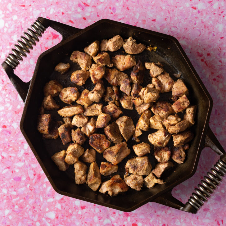 Carnitas browning in cast iron skillet.