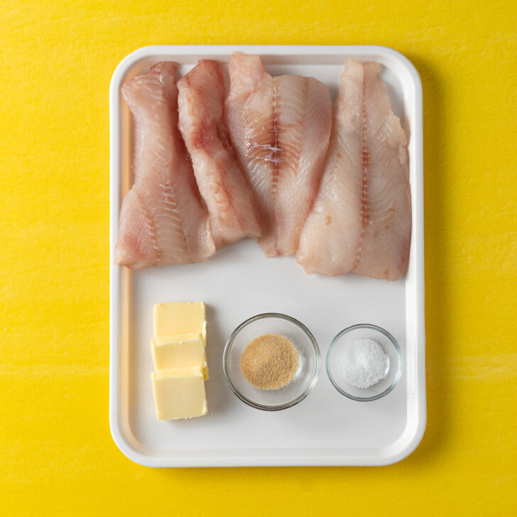 Sous vide cod ingredients on white tray on yellow background.