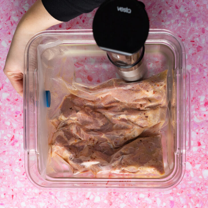 Vacuum sealed carnitas in sous vide water bath being secured with sous vide magnets.