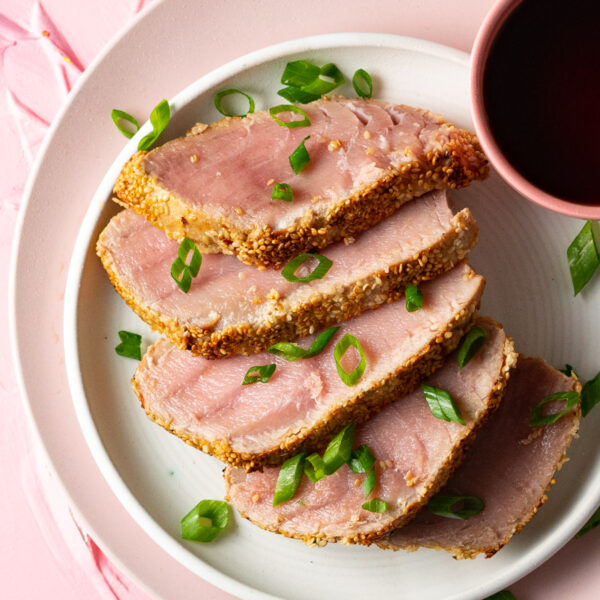 Sous vide tuna steak crusted with sesame seeds and sliced on a white plate with soy sauce.