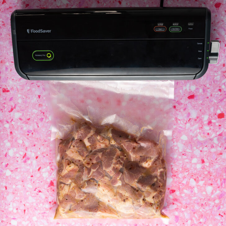 Pork shoulder and carnitas marinated being vacuum sealed on pink surface.