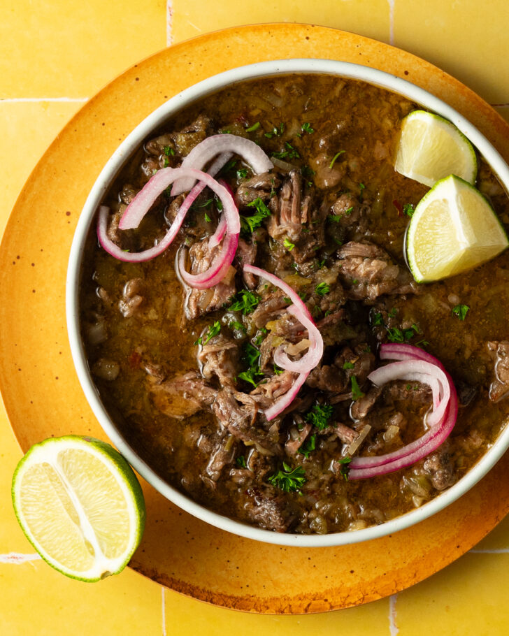 Sous vide barbacoa served in a bowl with red onions and limes on a yellow surface.
