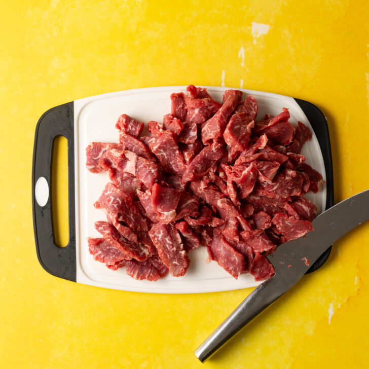 Sliced ribeye steak on white cutting board.