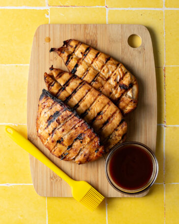 Grilled chicken breasts on cutting board with sauce.