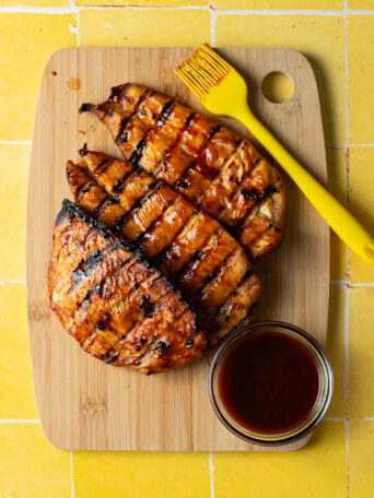 Grilled chicken breasts marinated in bbq chicken marinade on wood cutting board.