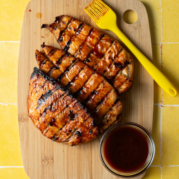 Grilled chicken breasts marinated in bbq chicken marinade on wood cutting board.